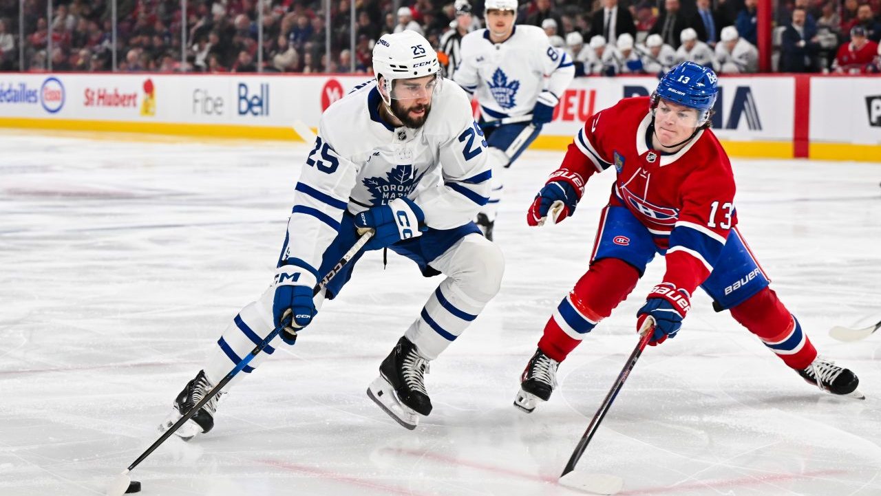 Conor Timmins of the Toronto Maple Leafs skates the puck against Cole Caufield of the Montreal Canadiens.